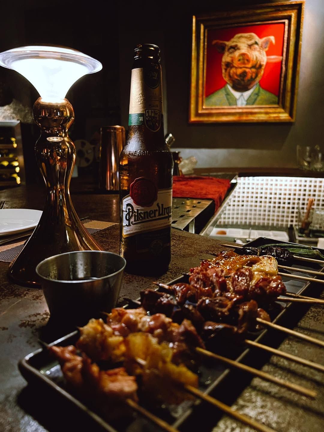 Grilled skewers and a beer at the bar under a pig portrait